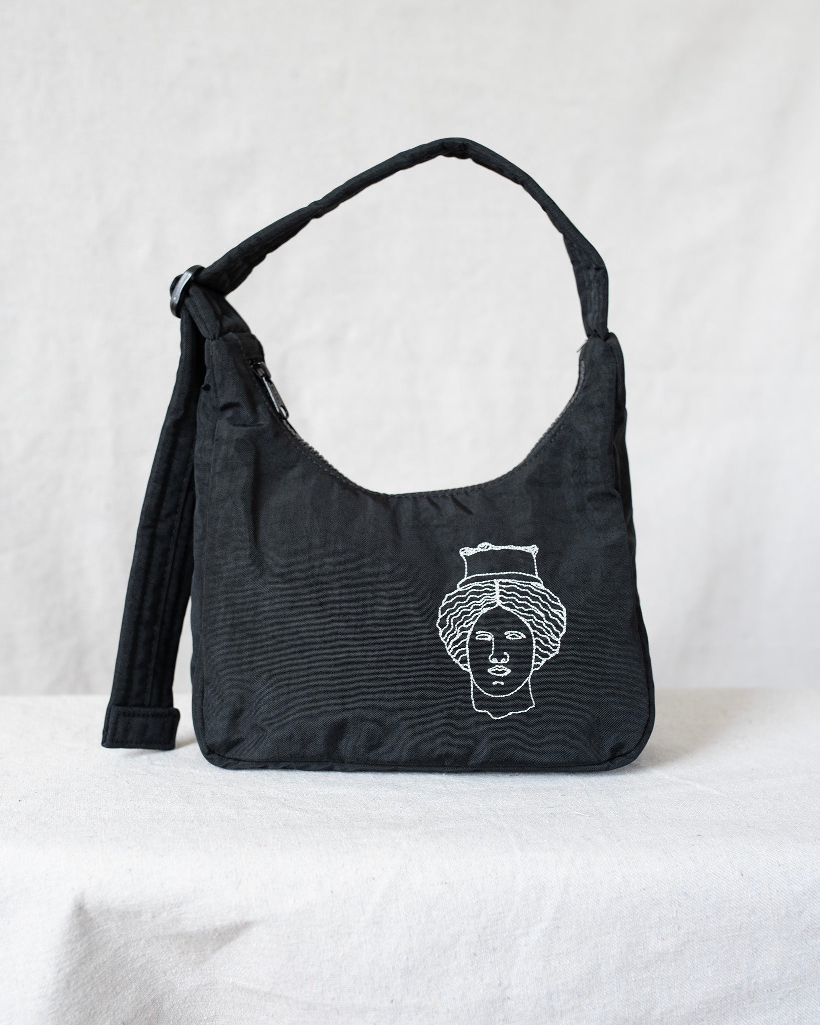 Black shoulder bag with white face design on a light gray background