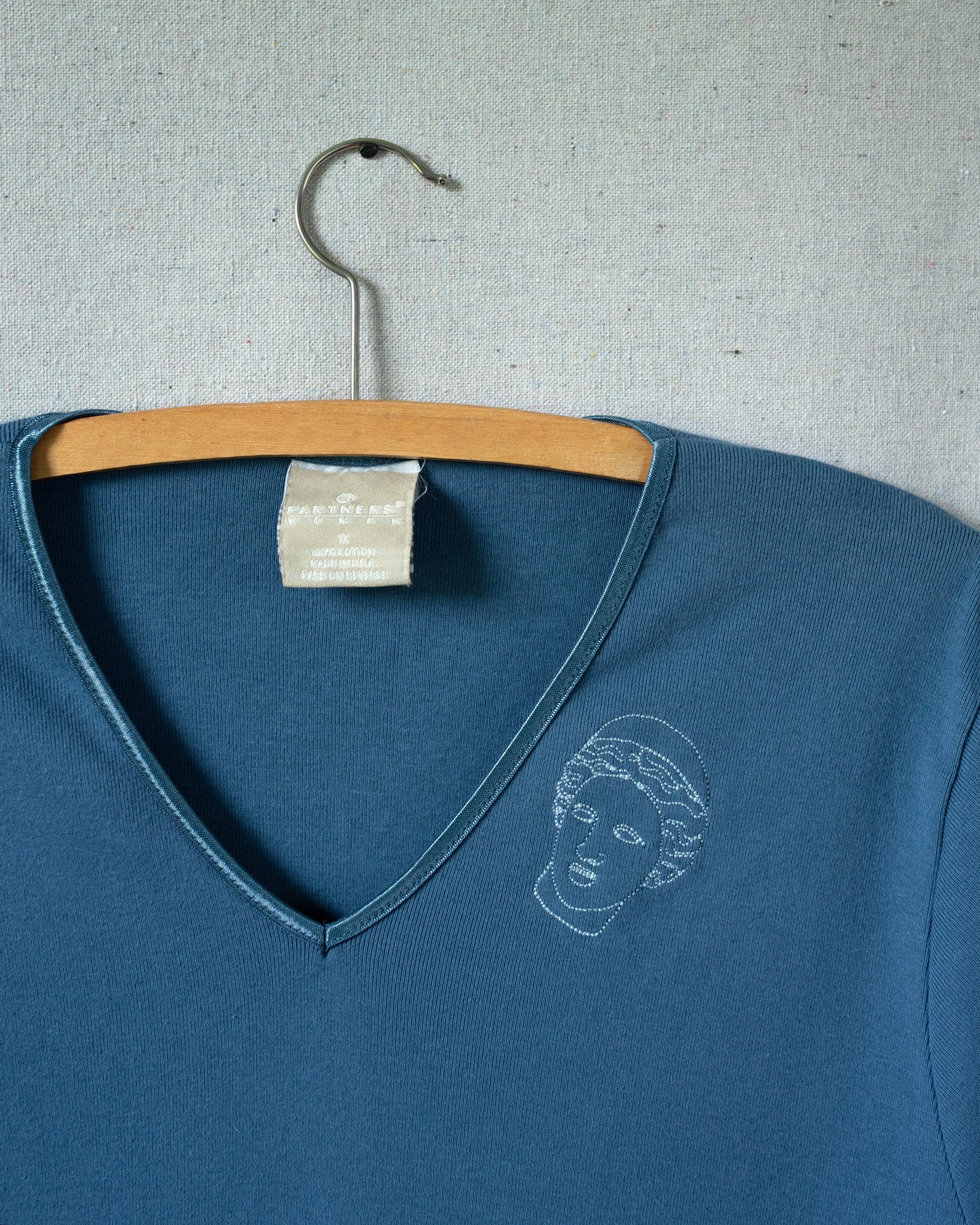 Blue V-neck shirt with a white graphic on a hanger against a gray background