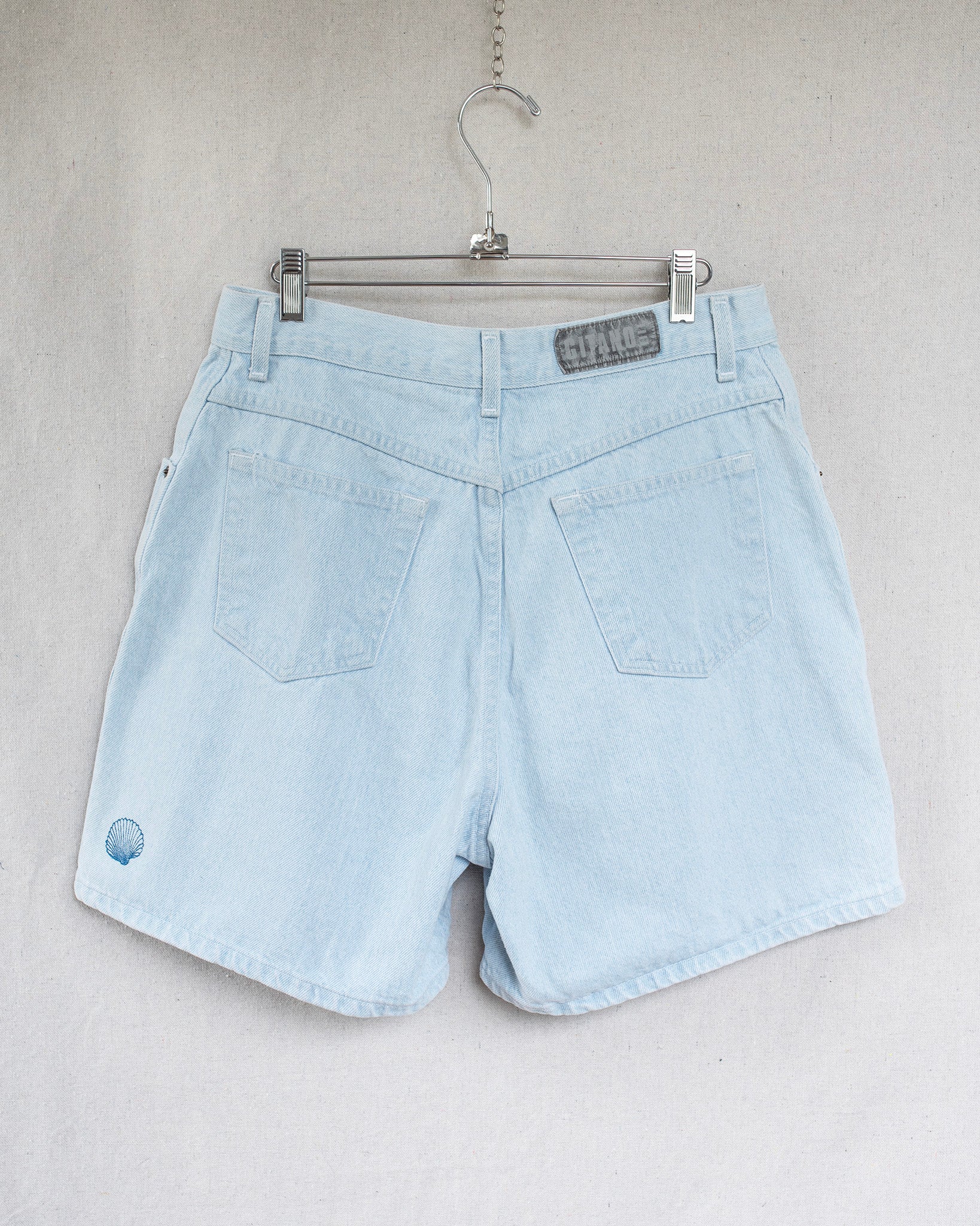 Light blue denim shorts on a hanger against a plain background