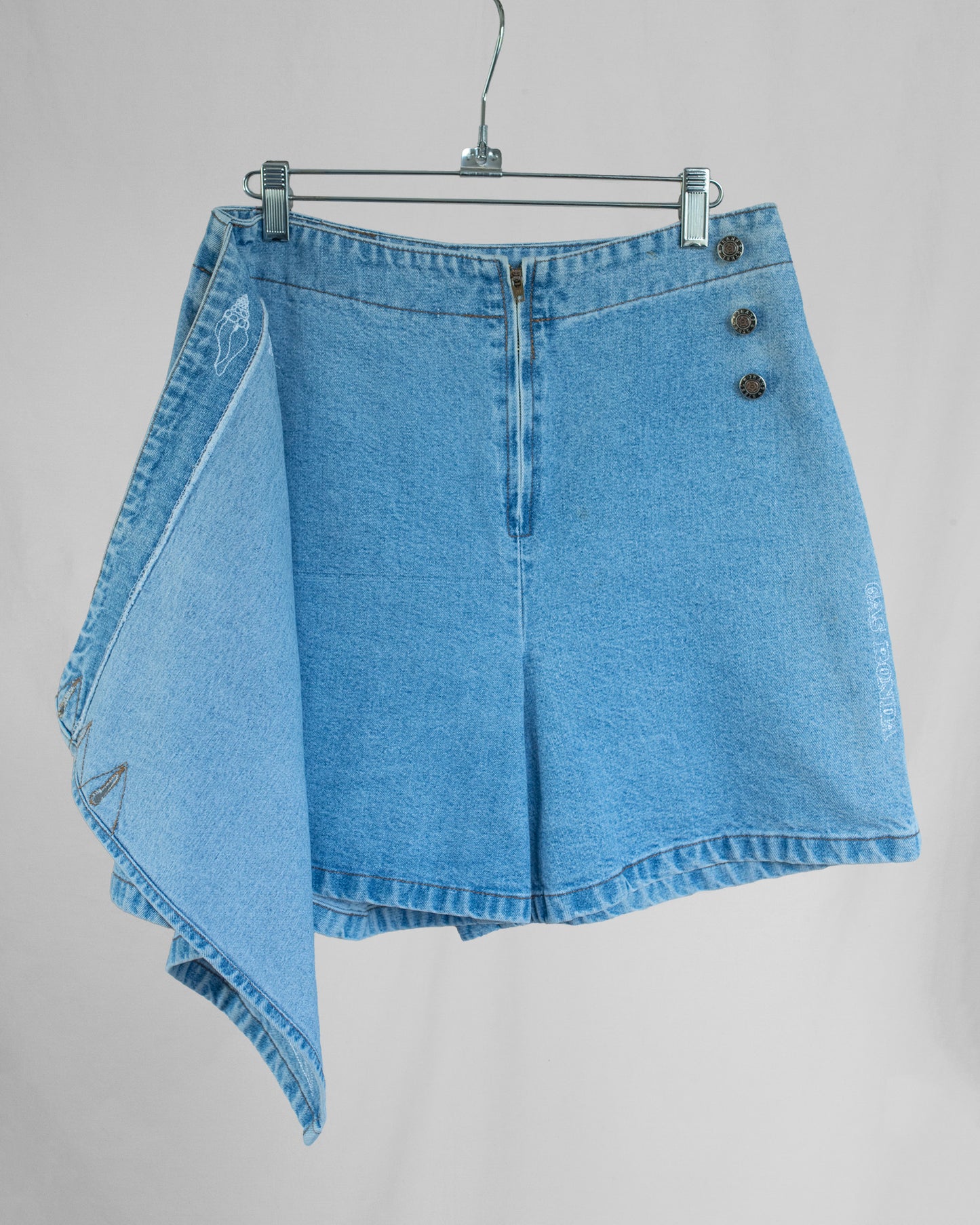 Blue denim skort on a hanger against a gray background