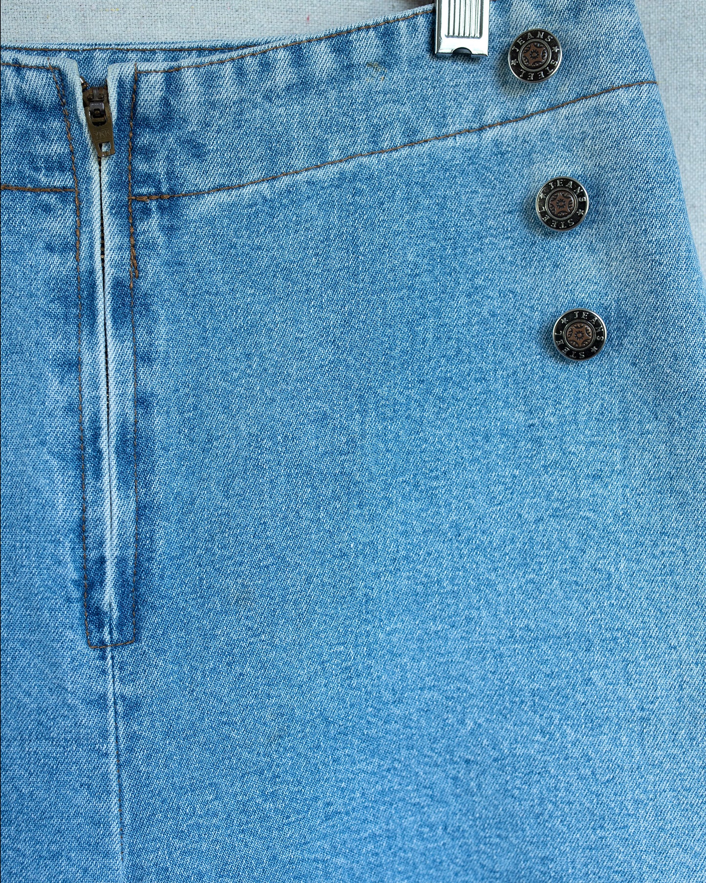Close-up of blue denim fabric with buttons and a zipper.