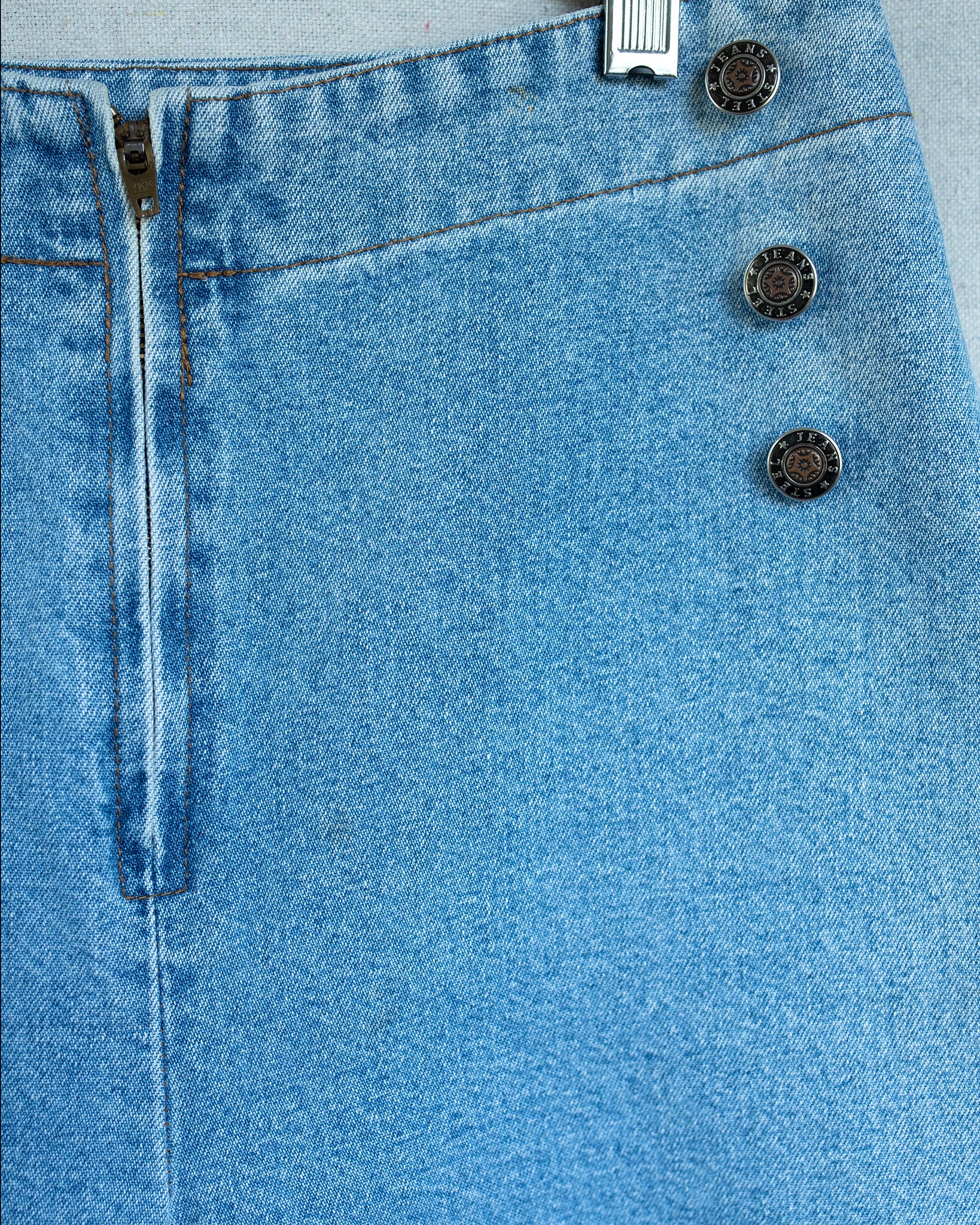 Close-up of blue denim fabric with buttons and a zipper.