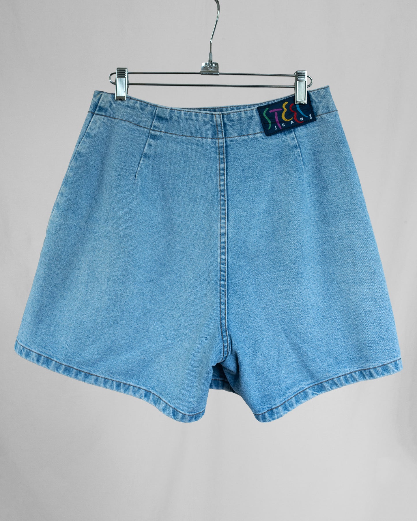 Blue denim skort on a hanger against a gray background