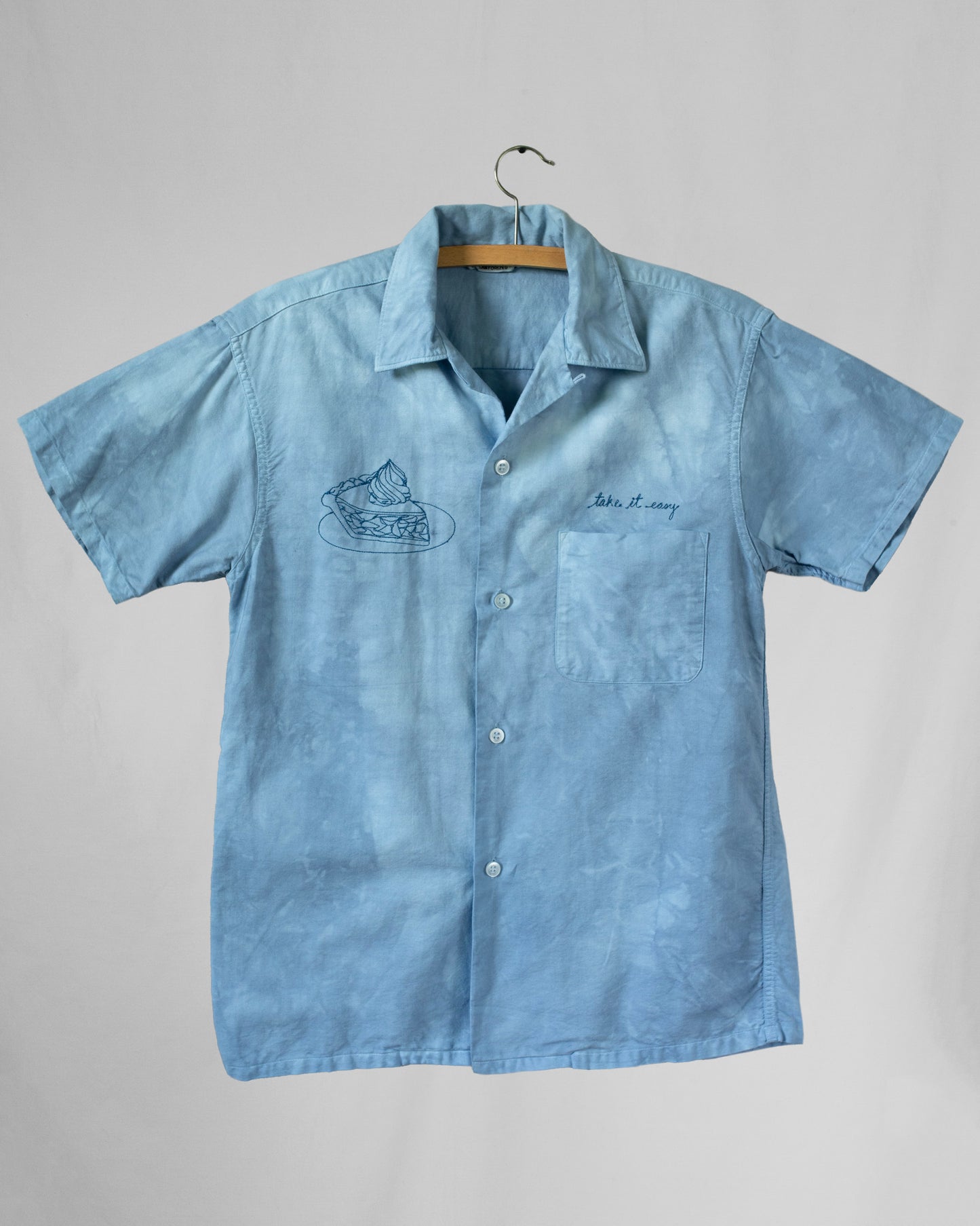Blue dyed shirt with embroideries displayed on a hanger