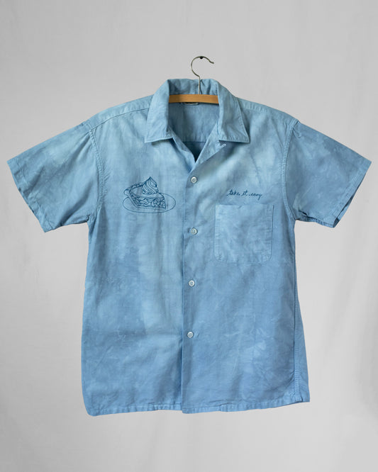 Blue dyed shirt with embroideries displayed on a hanger