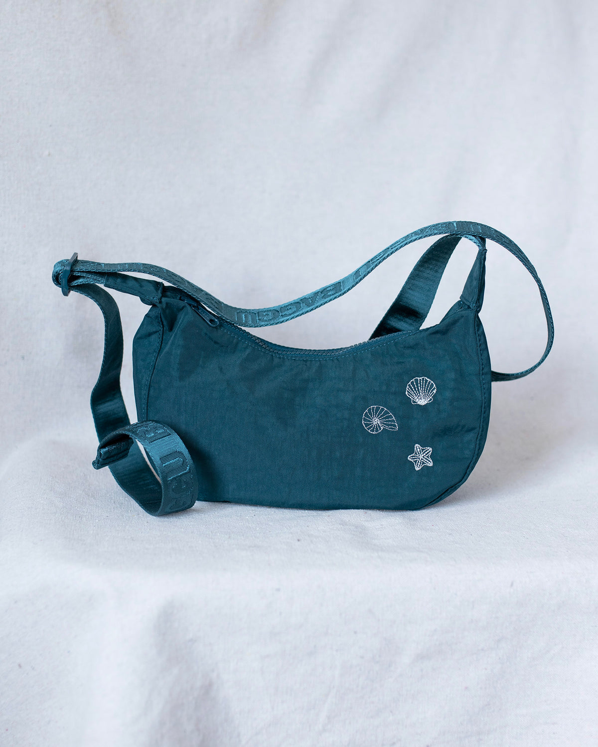 Baggu crossbody crescent bag with seashell embroideries against a white background.