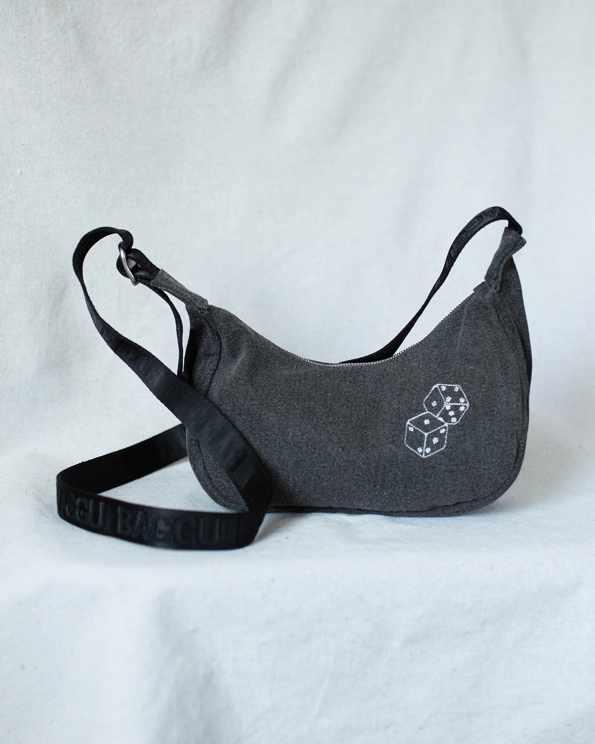 Black denim baggu smalll crescent bag with a dice embroidery against a white background.