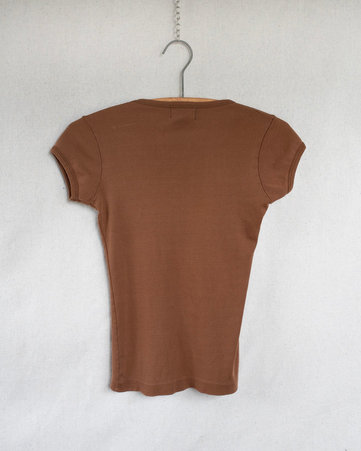 A brown short-sleeve ribbed knit top hanging on a wooden hanger against a light gray textured wall.