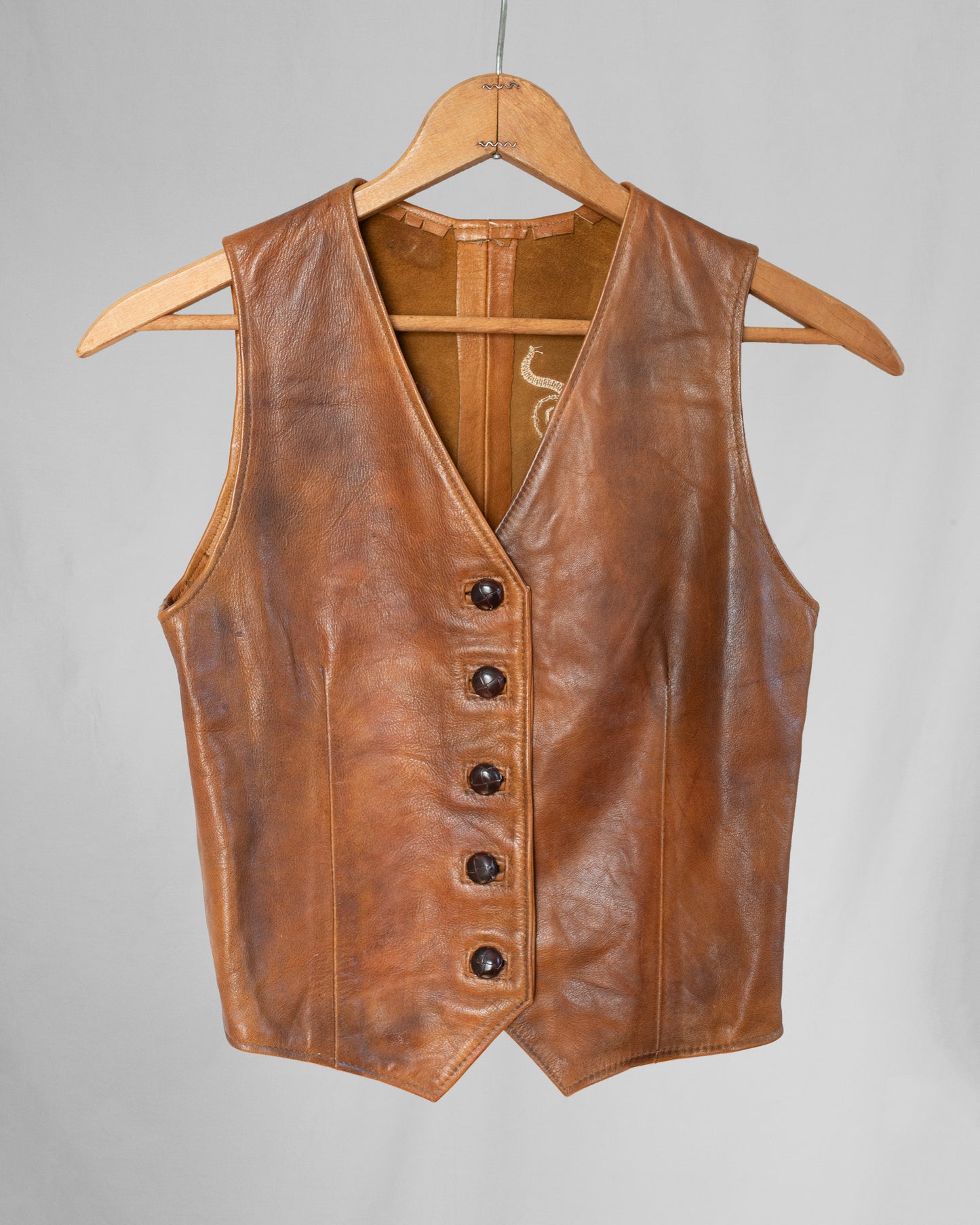 Brown leather vest on a hanger against a gray background