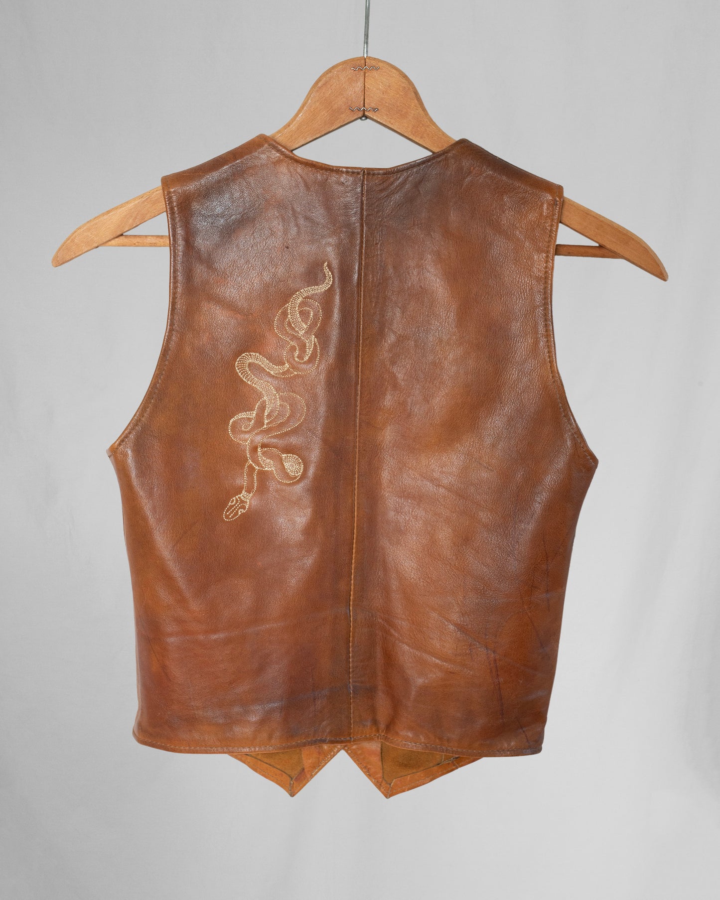 Brown leather vest with embroidery on a hanger against a gray background