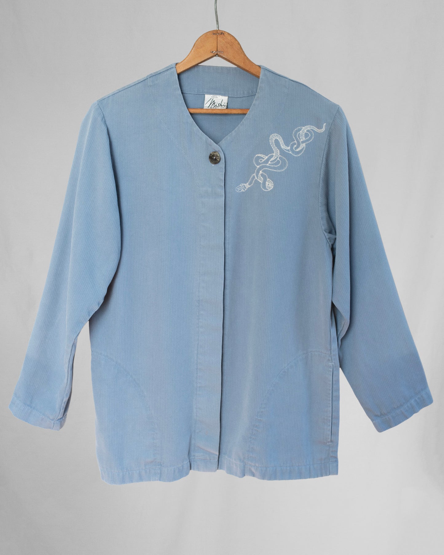 Light blue jacket with embroidery on a wooden hanger against a gray background