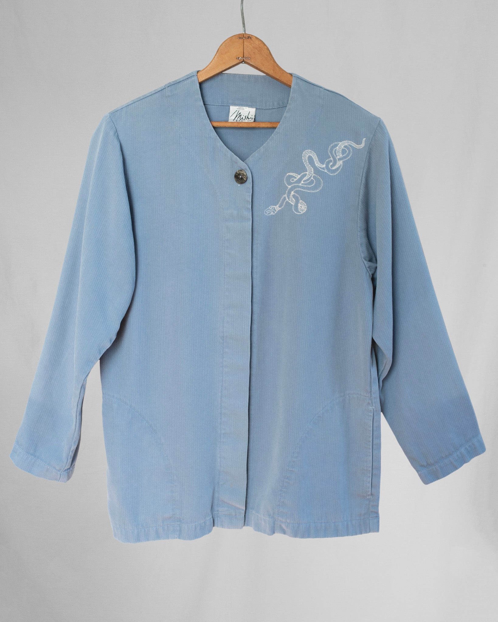 Light blue jacket with embroidery on a wooden hanger against a gray background