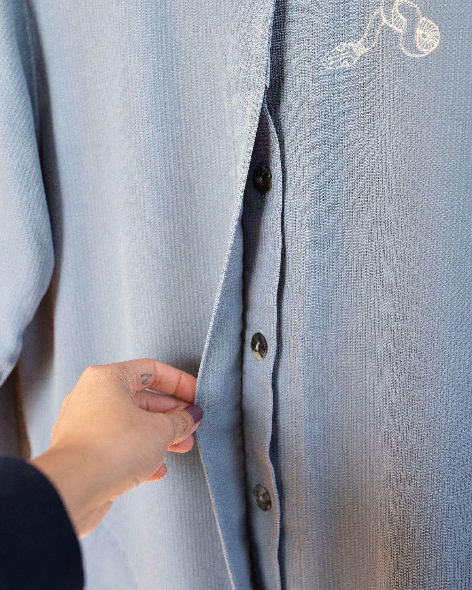 Light blue shirt with buttons being adjusted by a hand on a plain background