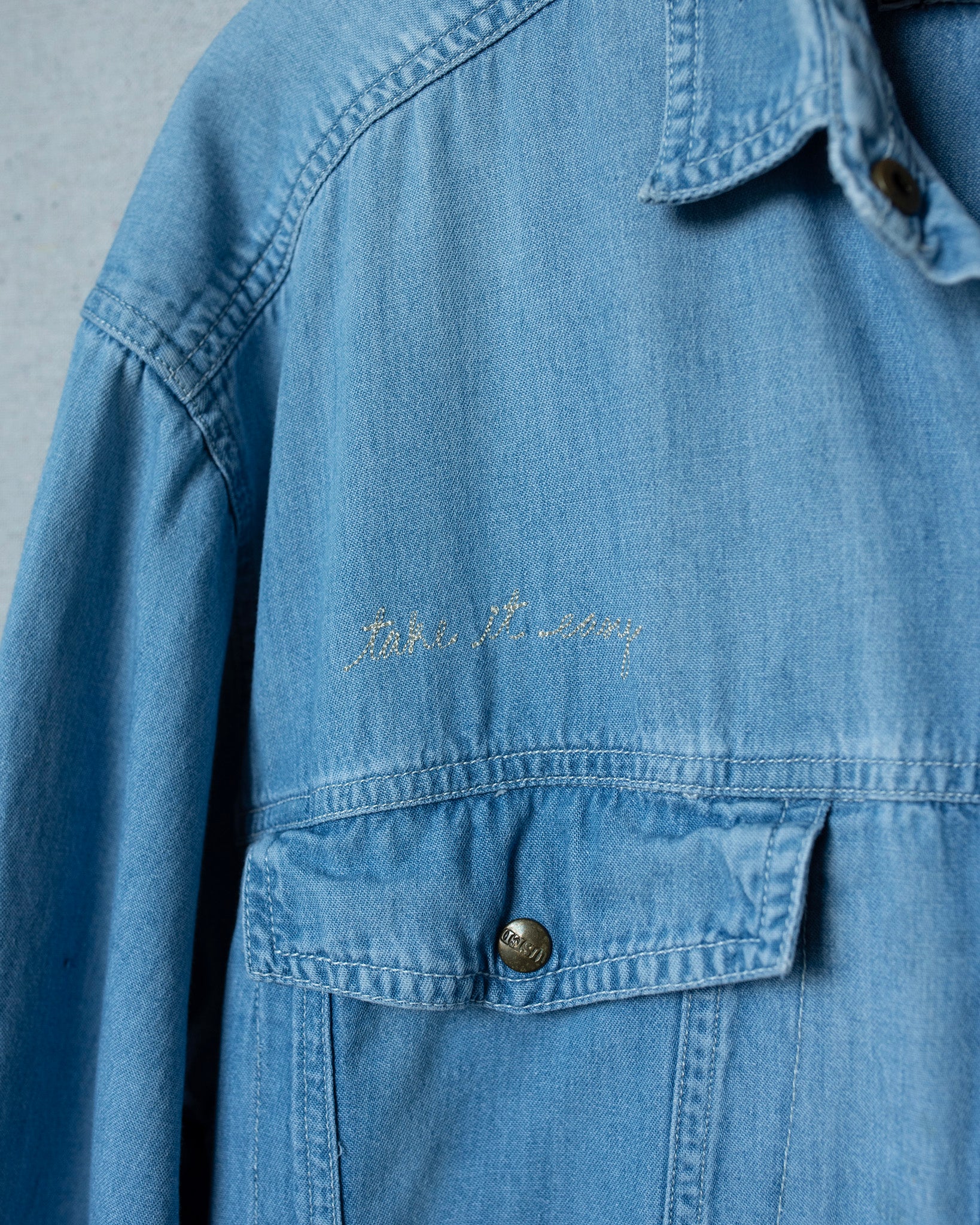 Blue denim jacket with text embroidery on a gray background