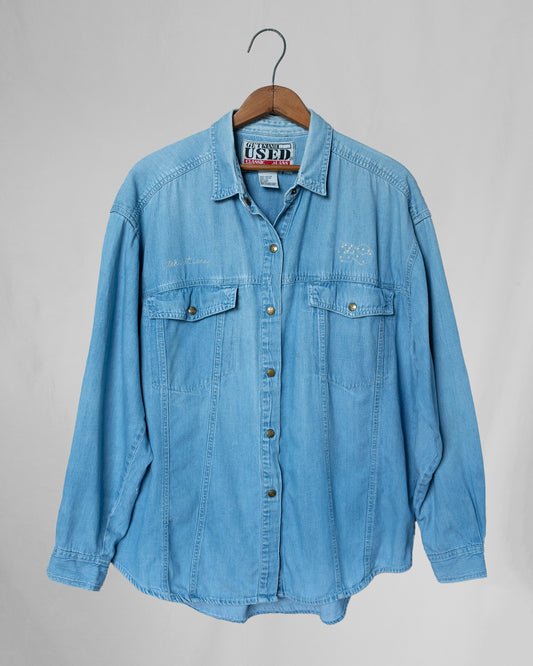 Light blue denim shirt on a hanger against a gray background