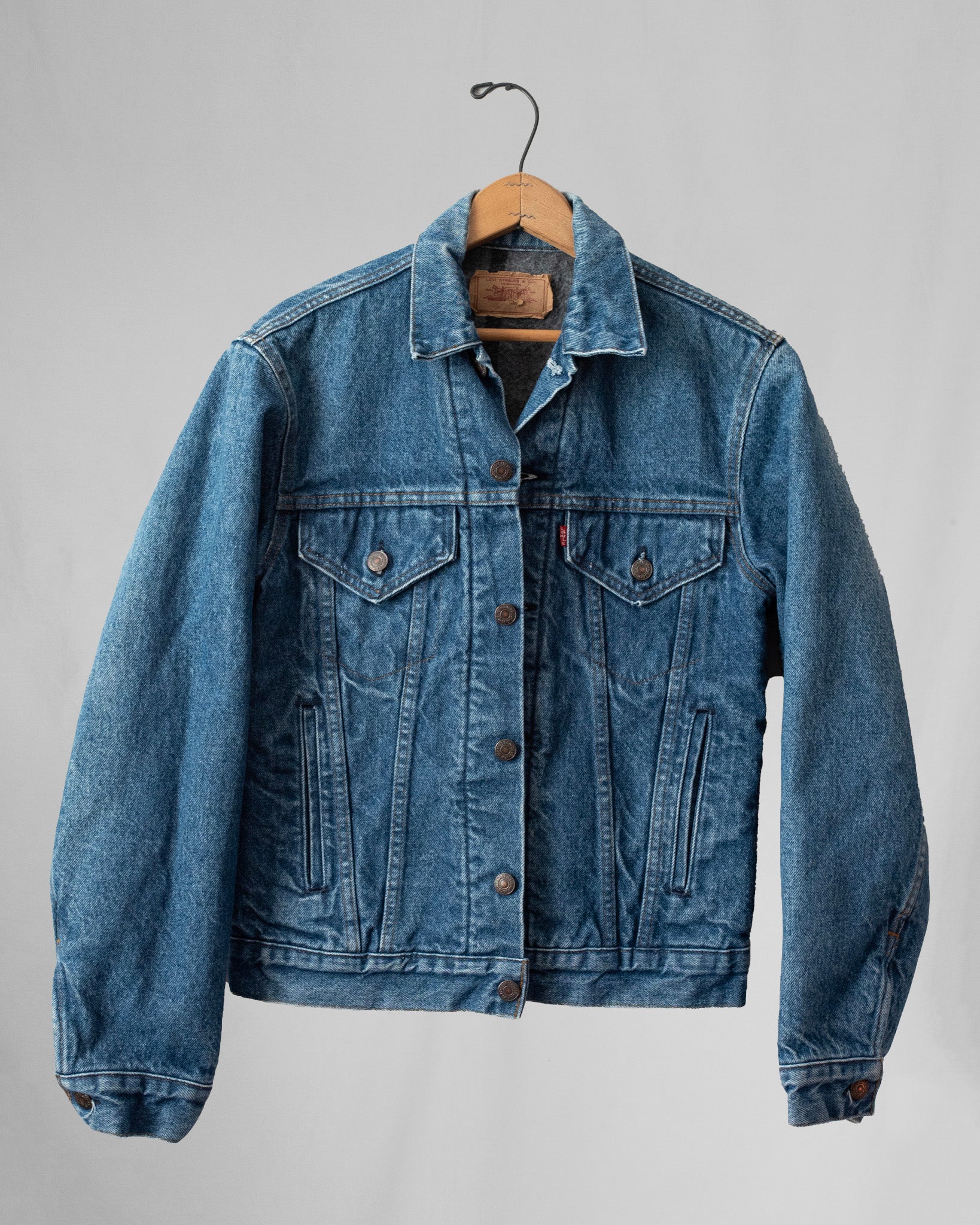 Blue denim jacket on a hanger against a gray background