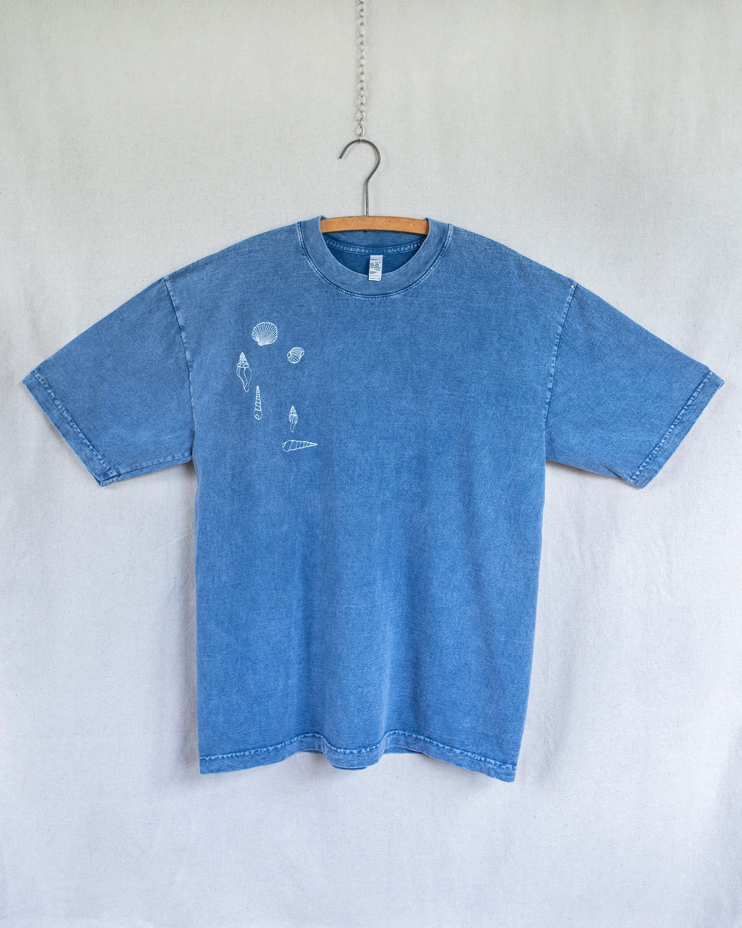 Blue t-shirt with seashells embroidered hanging on a white background