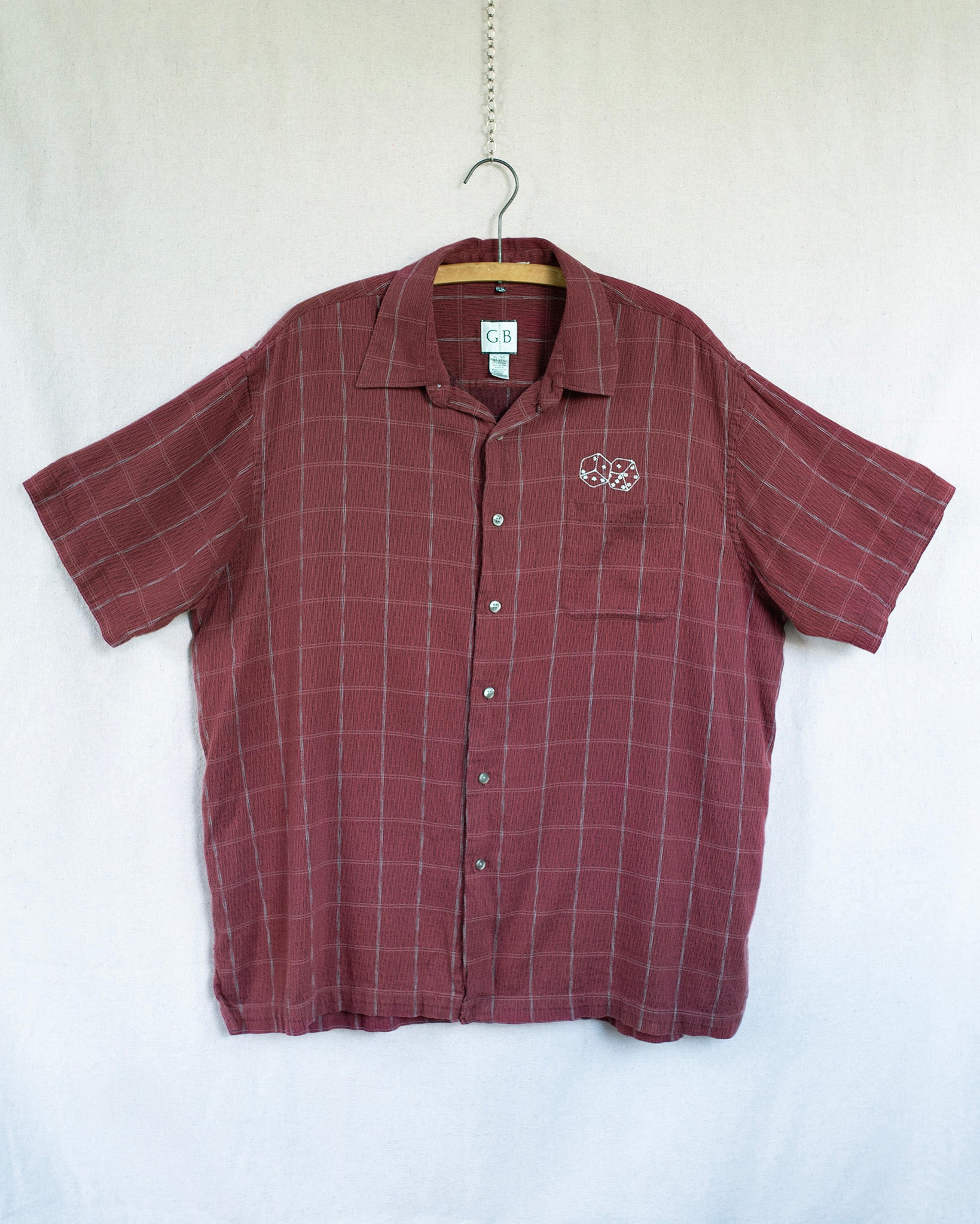 Maroon checkered shirt with a dice embroidery on a hanger against a white background