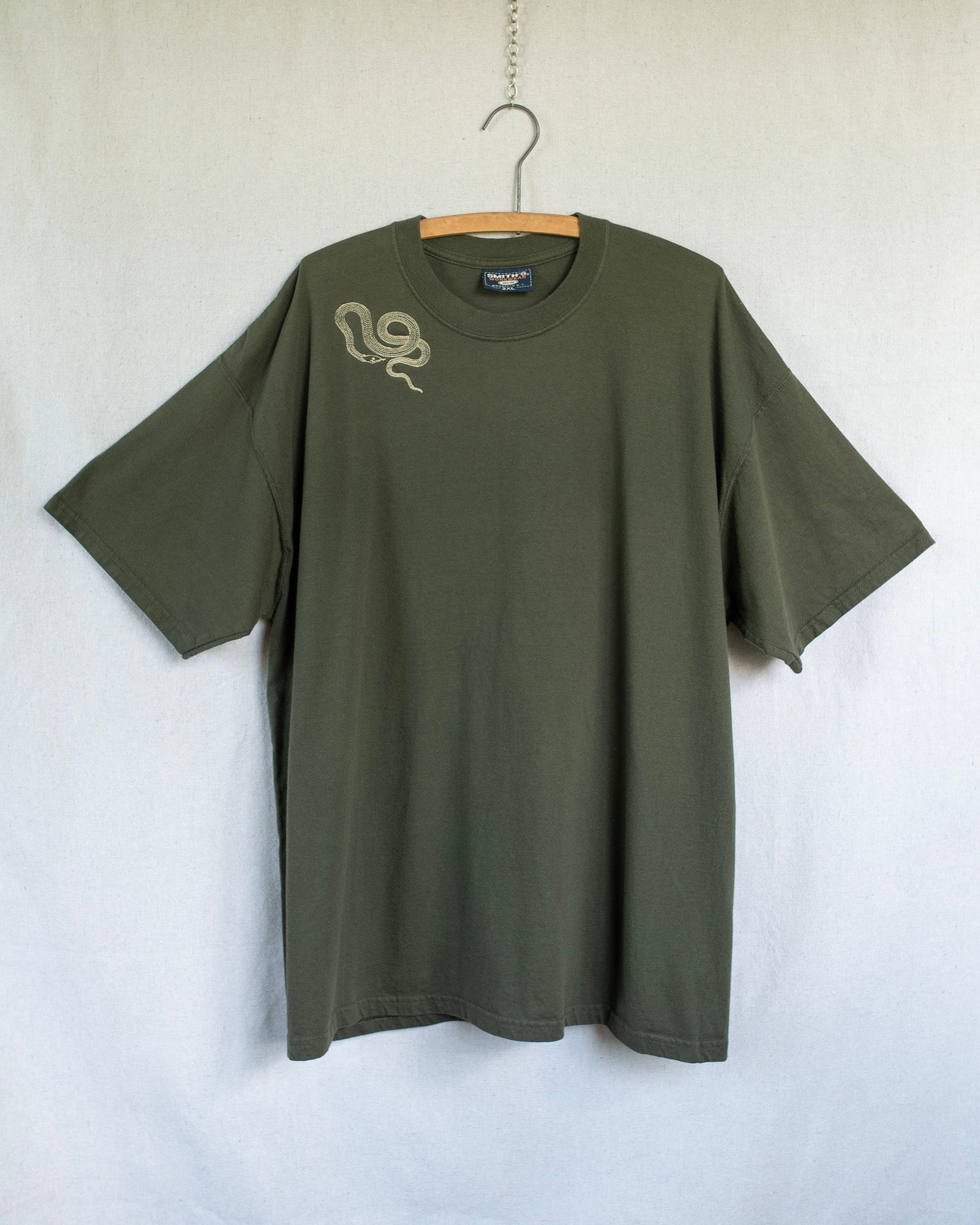 Green t-shirt with a snake embroidery on a hanger against a white background