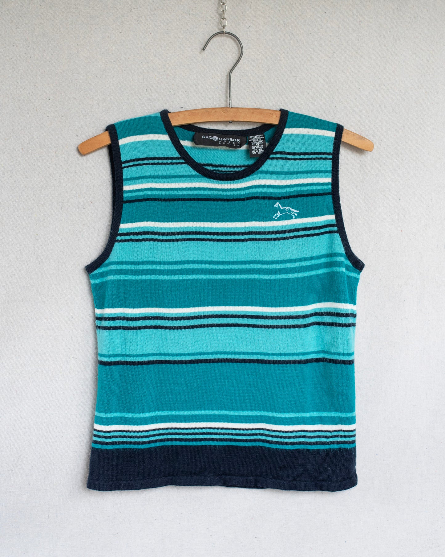 A sleeveless striped tank top hanging on a wooden hanger against a light gray wall. The top features horizontal stripes in teal, light blue, white, and dark navy, with a small white horse embroidery on the left chest.