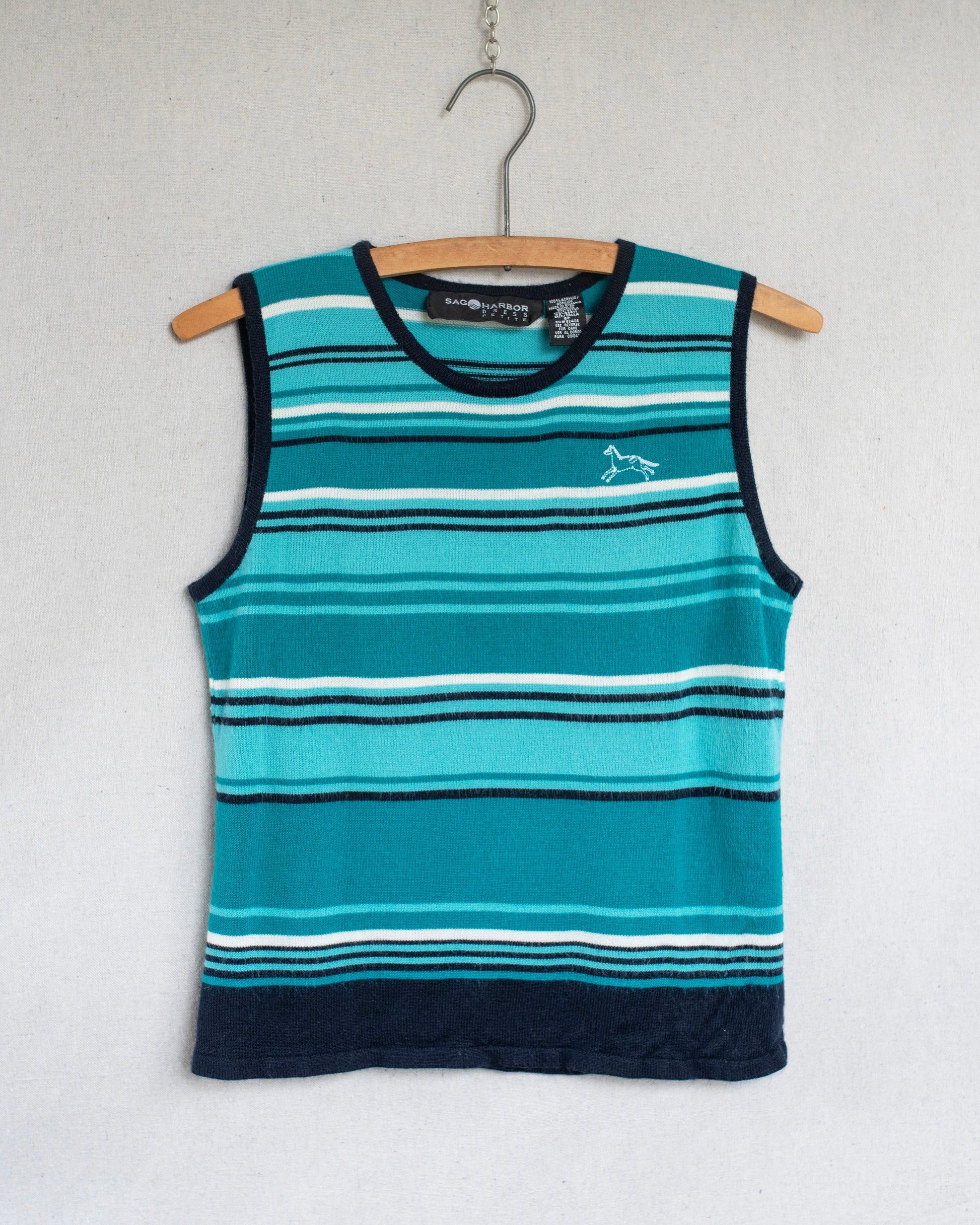 A sleeveless striped tank top hanging on a wooden hanger against a light gray wall. The top features horizontal stripes in teal, light blue, white, and dark navy, with a small white horse embroidery on the left chest.