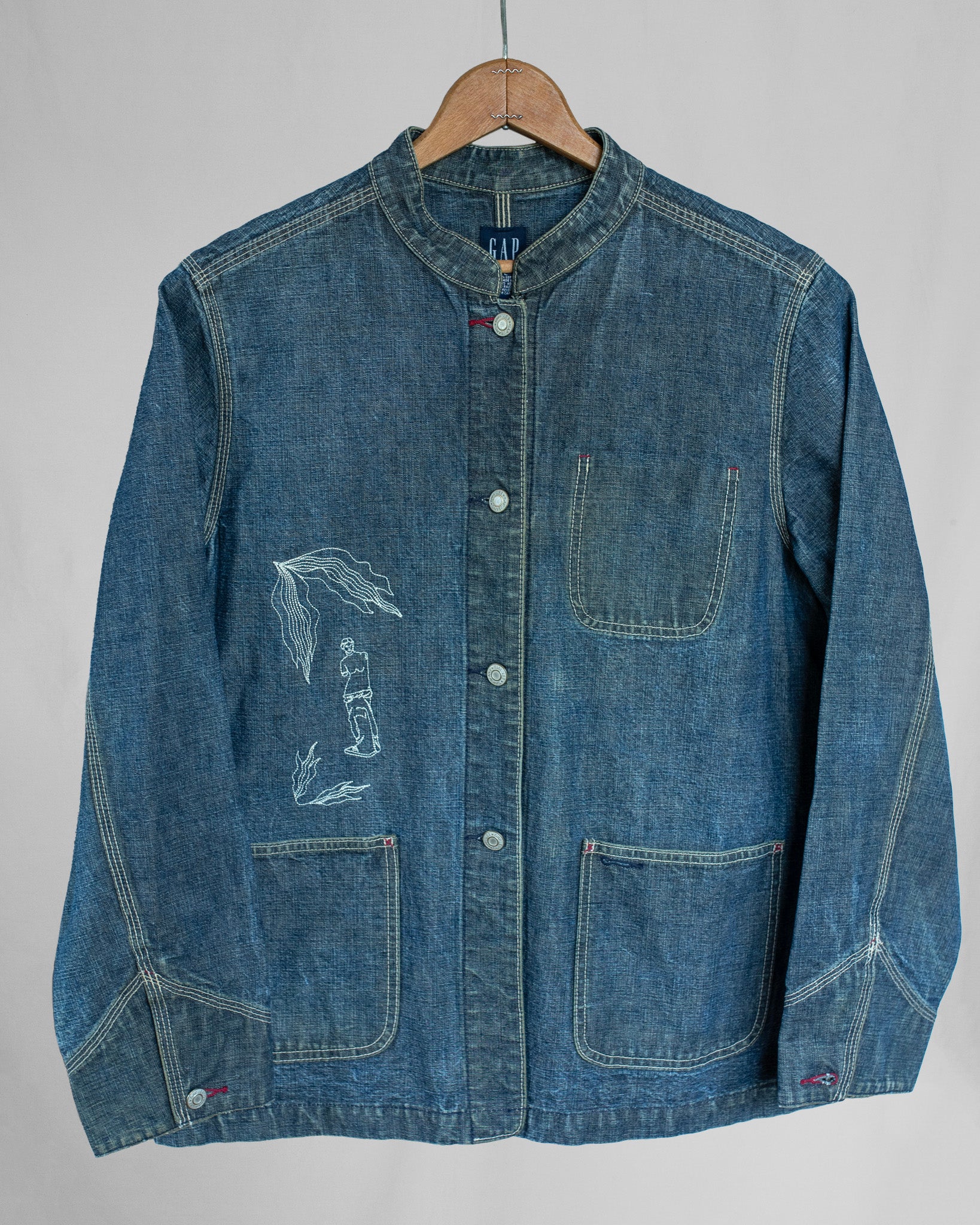 Blue denim jacket with embroideries on a hanger against a gray background