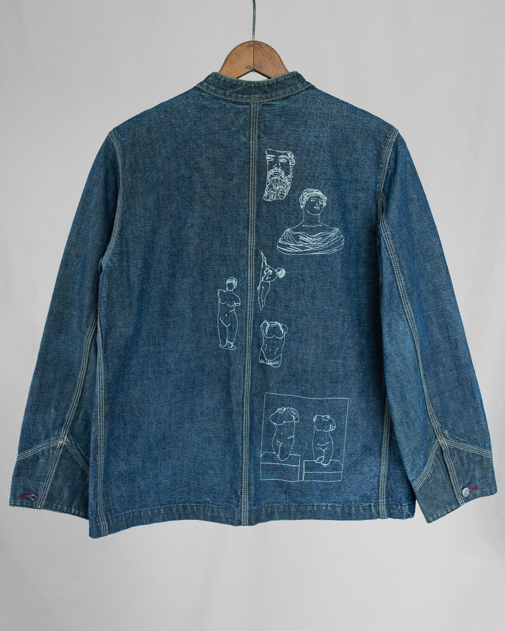 Blue denim jacket with white embroidered designs on a gray background